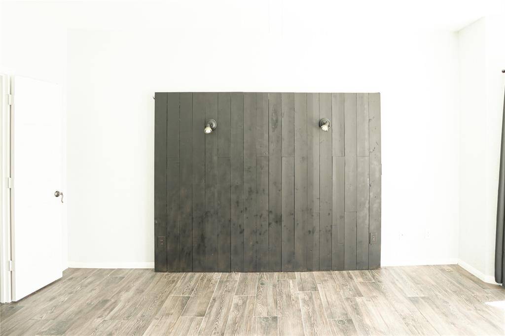 This room features a modern accent wall with dark wood paneling and two light fixtures. It has light-colored walls, wood-style flooring, and a door on the left, offering a clean and contemporary aesthetic.