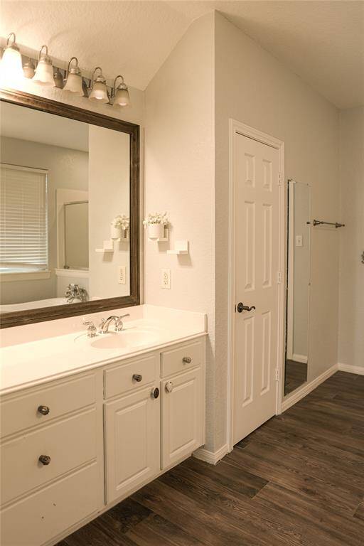 This bathroom features a large vanity with ample storage, a wide mirror with modern lighting, and elegant wood-look flooring. The neutral color palette complements the space, creating a cozy yet stylish atmosphere.