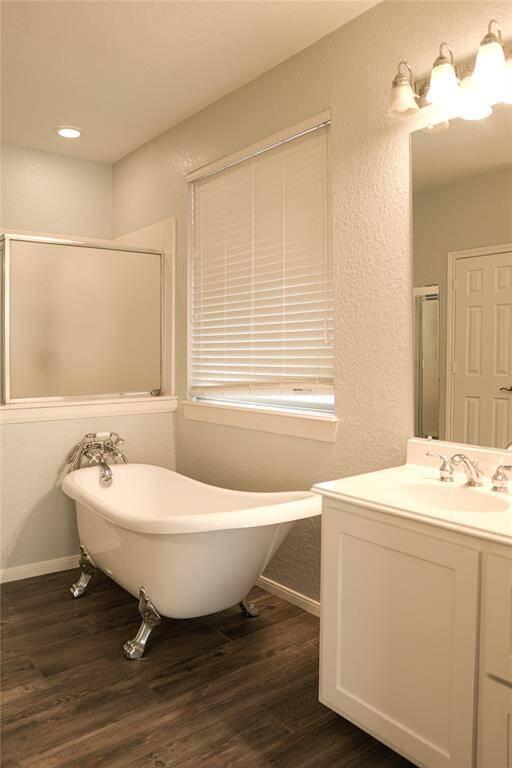 This bathroom features a classic clawfoot bathtub, sleek vanity, and elegant lighting. The space has a modern yet cozy feel with neutral tones and wood-look flooring. A window with blinds provides natural light and privacy.