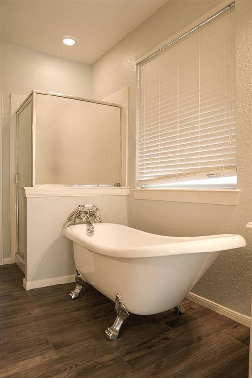 This bathroom features a classic clawfoot bathtub and a separate shower. The room has a modern feel with wood-style flooring and a large window with blinds, providing ample natural light.