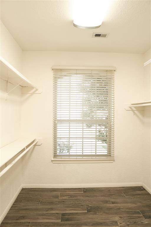 This is a bright walk-in closet with ample shelving on both sides, a large window with blinds, and wood-look flooring.