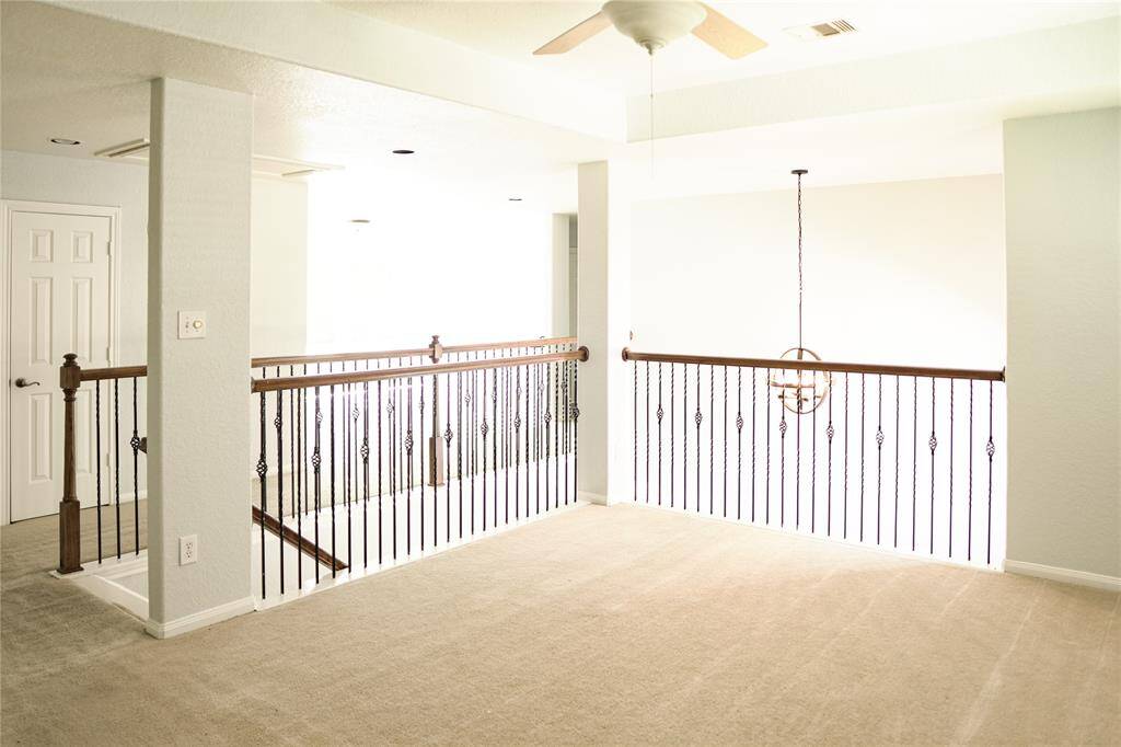 This photo showcases a bright, open upstairs landing with carpet flooring, a ceiling fan, and decorative iron railings. It features a neutral color scheme and receives ample natural light.