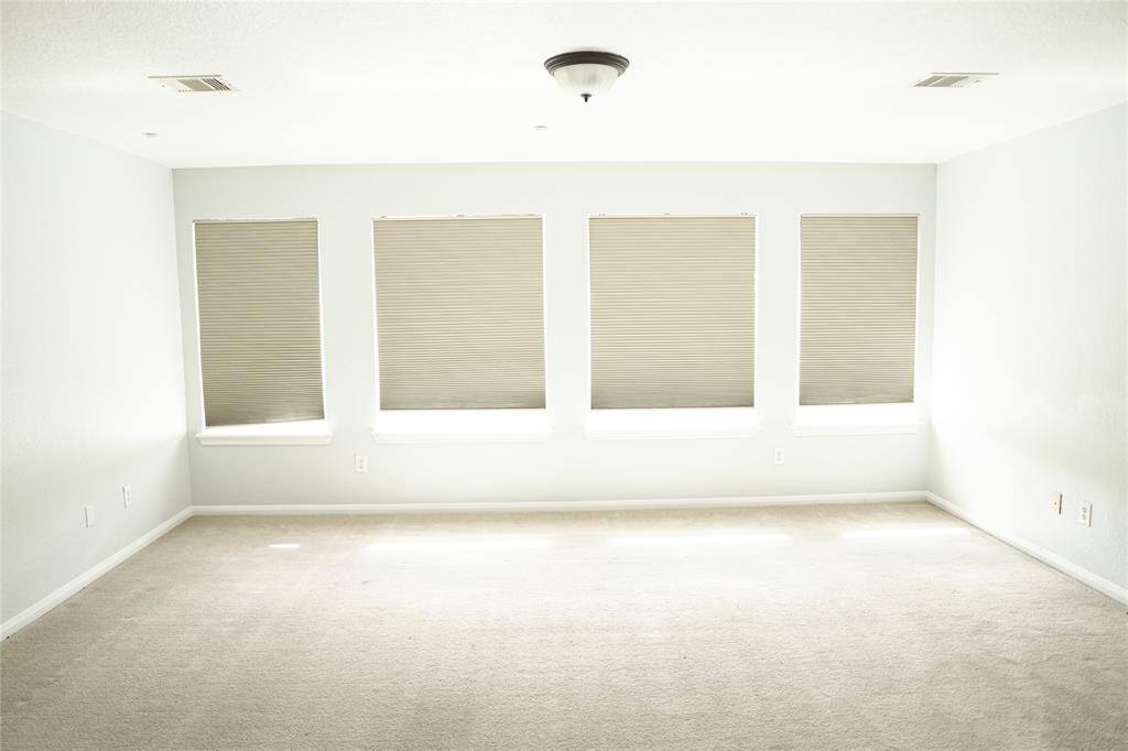 Bright, spacious room with neutral walls and carpet. Features five large windows with blinds, allowing ample natural light. Clean and versatile space suitable for various uses.