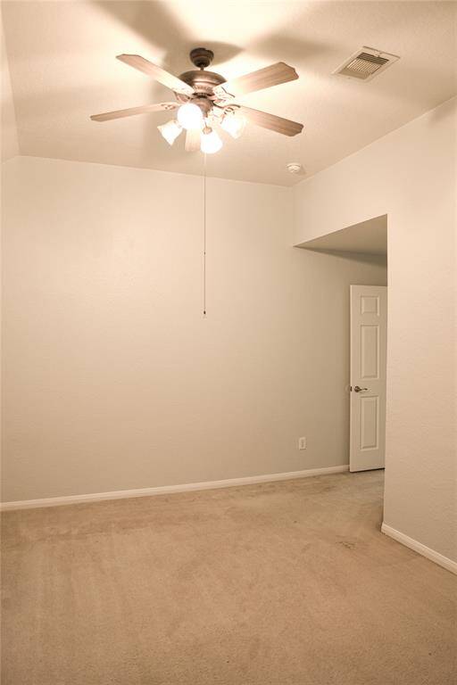 This room features neutral carpet and walls, a ceiling fan with lights, and a small entryway with a door, offering a blank canvas for customization.