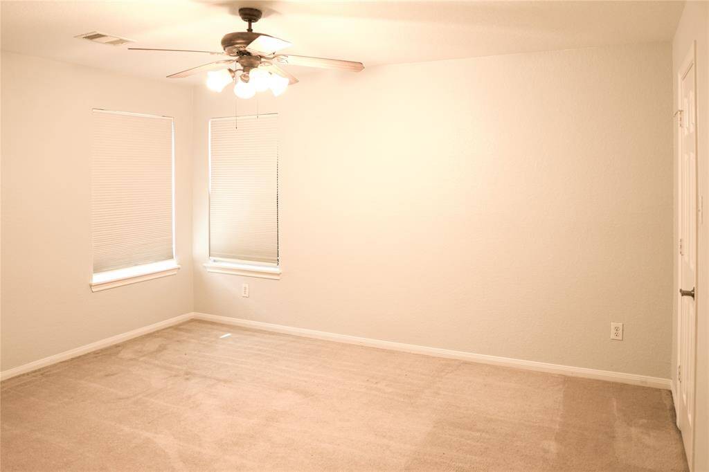 This is a bright, empty room with neutral walls and carpet. It features two windows with blinds and a ceiling fan with lights, providing a simple and clean space ready for customization.