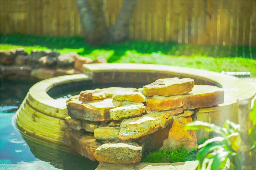 This photo showcases a serene backyard with a stone-lined hot tub adjacent to a pool. The natural stone accents and lush greenery create a relaxing, inviting atmosphere perfect for leisure and entertaining.