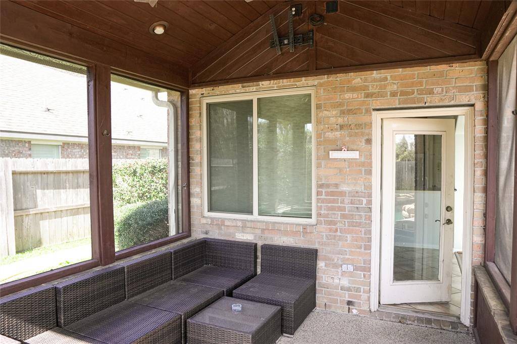 This photo shows a cozy screened-in porch with a wicker sectional sofa, brick walls, and a door leading to the yard. It's a great space for outdoor relaxation while being protected from the elements.