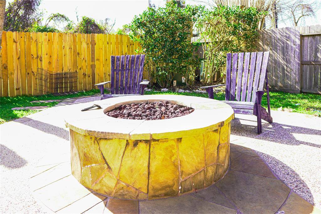 This backyard offers a cozy outdoor space with a stone fire pit, surrounded by two Adirondack chairs. It's enclosed by a wooden fence, providing privacy and a welcoming area for relaxation or entertaining.