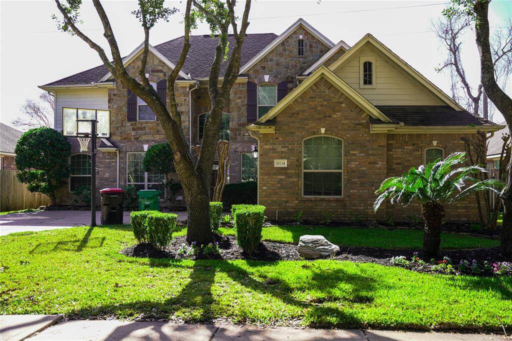 This charming two-story brick home features a well-maintained front yard with lush landscaping and mature trees. The exterior boasts a traditional design with a gabled roof and multiple windows, providing plenty of natural light. A driveway leads to an attached garage, offering convenient parking.