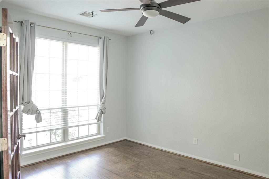 This room features a large window with light curtains, offering plenty of natural light. It has hardwood flooring, a ceiling fan, and neutral-colored walls, providing a bright and airy feel.