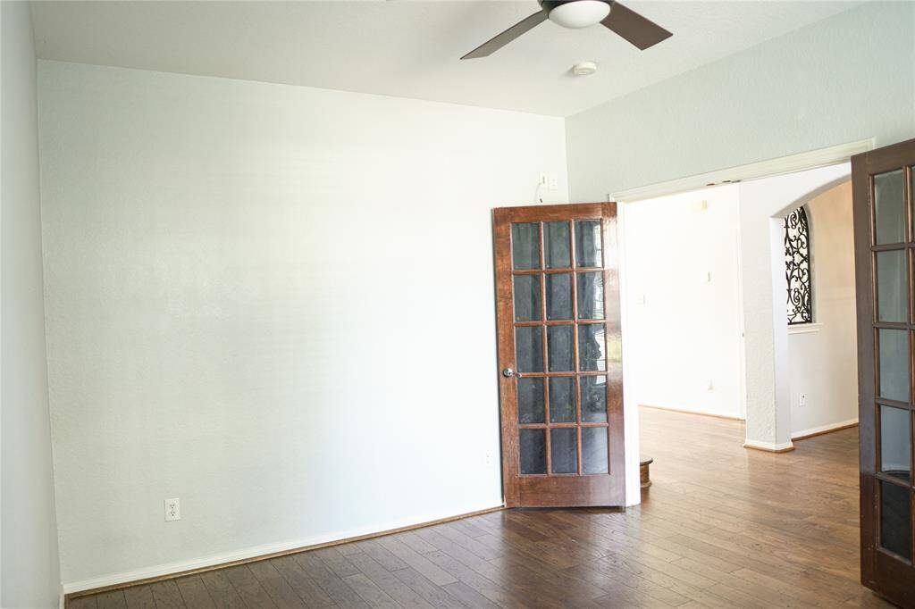 This room features hardwood floors, a ceiling fan, and French doors leading to an adjacent space. The neutral walls enhance natural light, creating an inviting and versatile area.