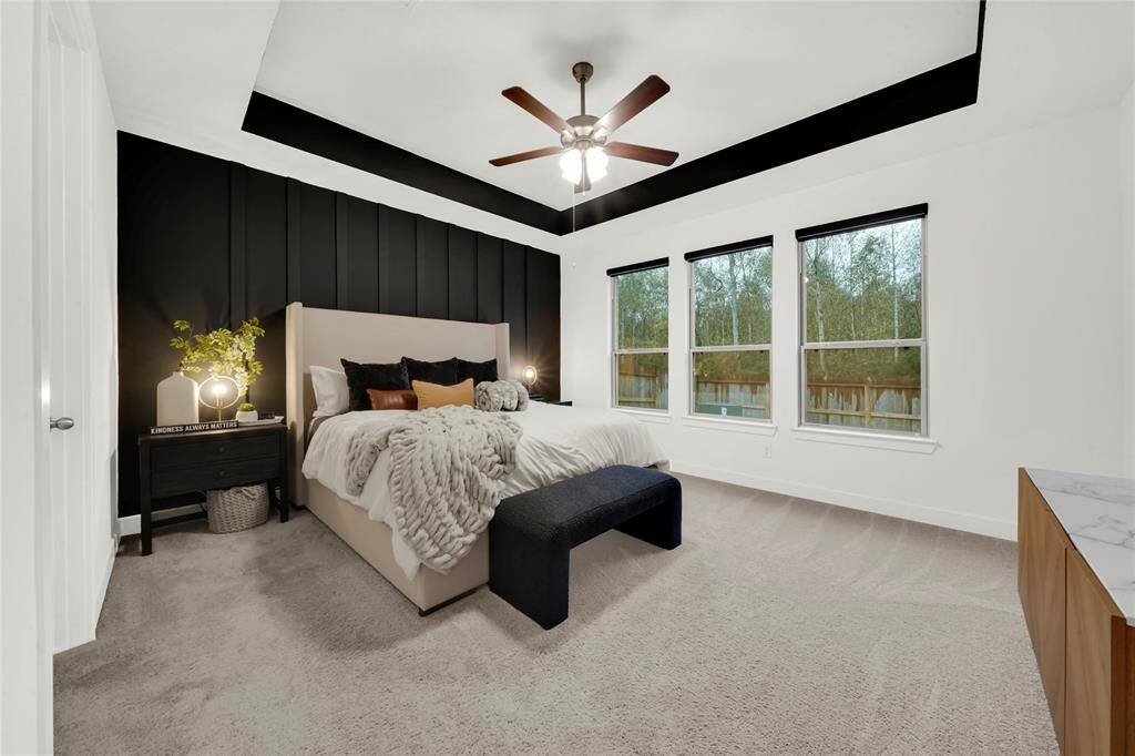 This spacious bedroom features a modern design with a stunning accent wall and ceiling trim. It provides ample natural light from three large windows overlooking the back area and also boasts power window blinds.