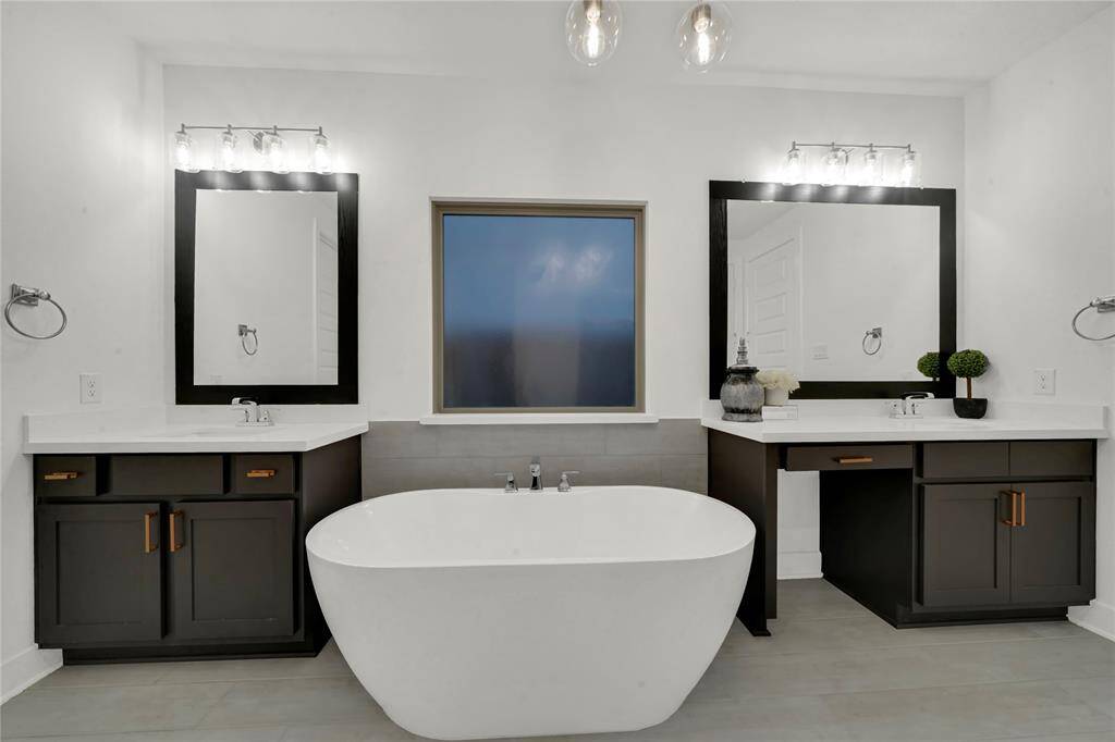 This bathroom features a modern design with a freestanding tub, dual vanities with dark cabinetry, and large framed mirrors. The space is well-lit with contemporary fixtures and has a central frosted window.