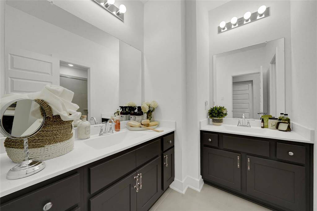 This upstairs bathroom features dual sinks with dark cabinetry, sleek countertops, and ample lighting.