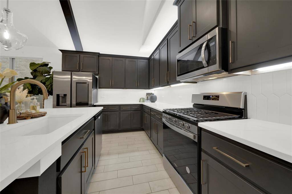 Modern kitchen with sleek dark cabinets, stainless steel appliances, and white quartz countertops.