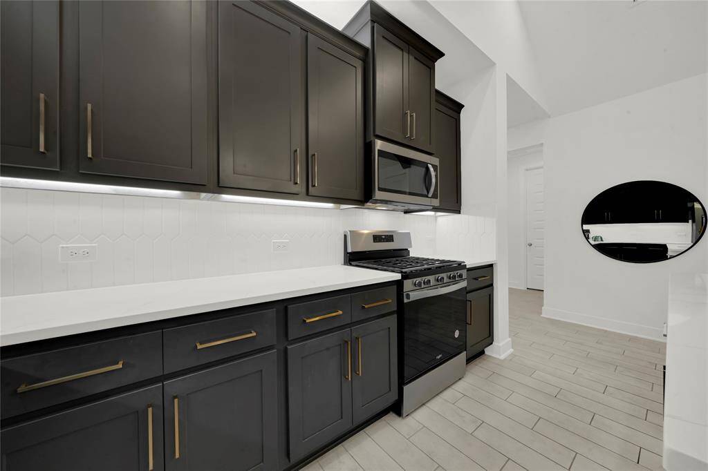 Another view of this bright, beautiful kitchen with stylish dark cabinetry against the light quartz countertops and upgraded backsplash