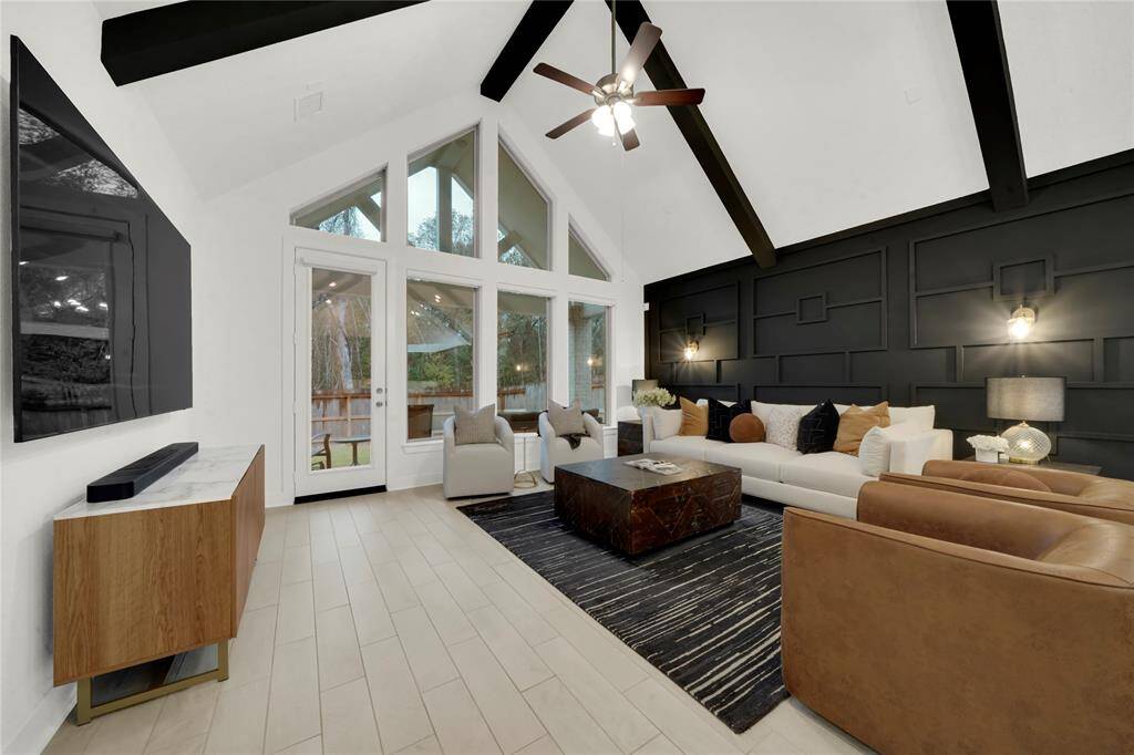 This living room features a vaulted ceiling with dark exposed beams and a striking accent wall. It has large windows and a glass door opening to a private outdoor space. The elegant lighting adds to the contemporary style.