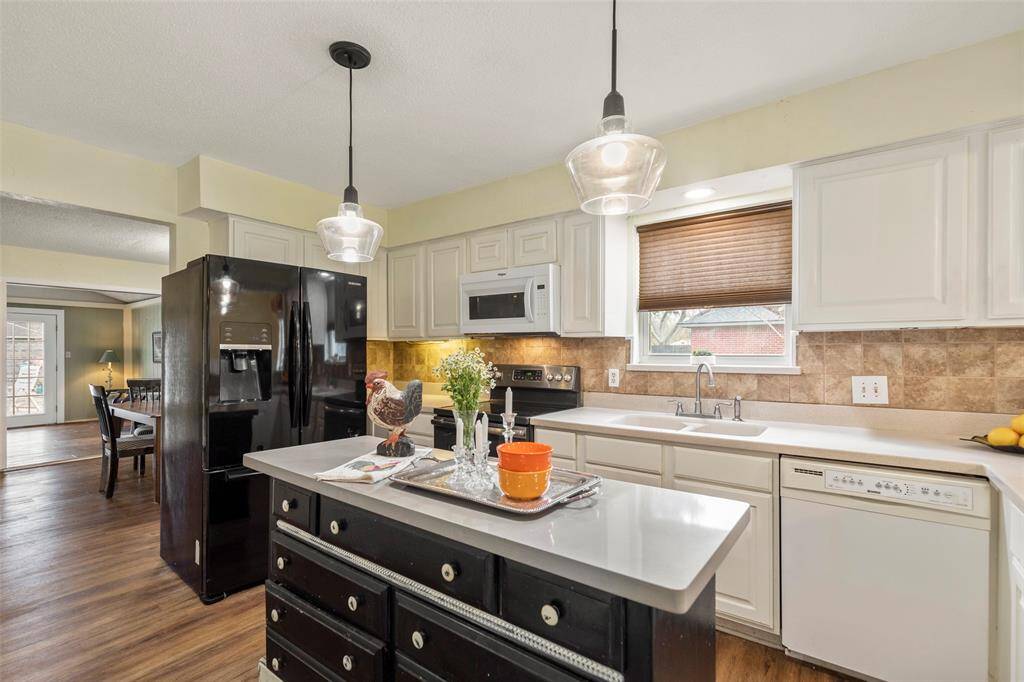 Well-appointed kitchen features island with decorative lighting, Corian countertops with tile backsplash, built-in cabinetry and drawers, electric stove/oven, microwave, dishwasher and refrigerator.
