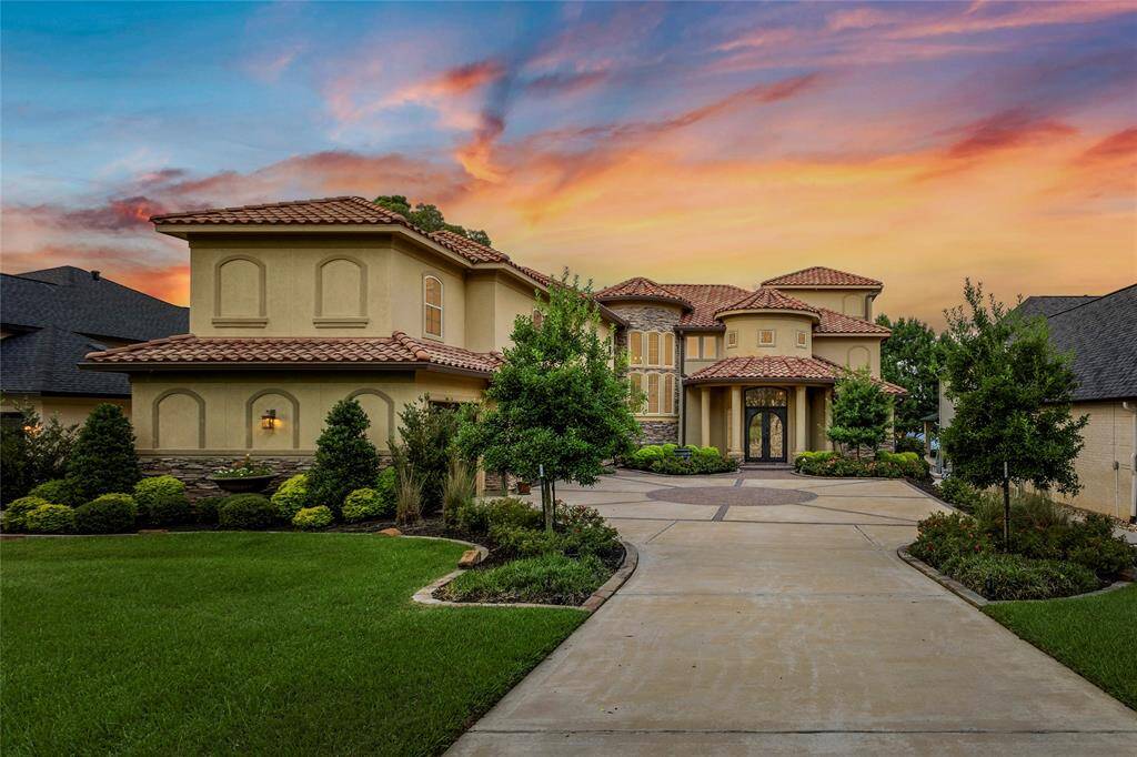 A luxurious backyard oasis with an inviting pool, elegant landscaping, and a covered patio, all overlooking a serene lakeside view under a vibrant sunset sky.