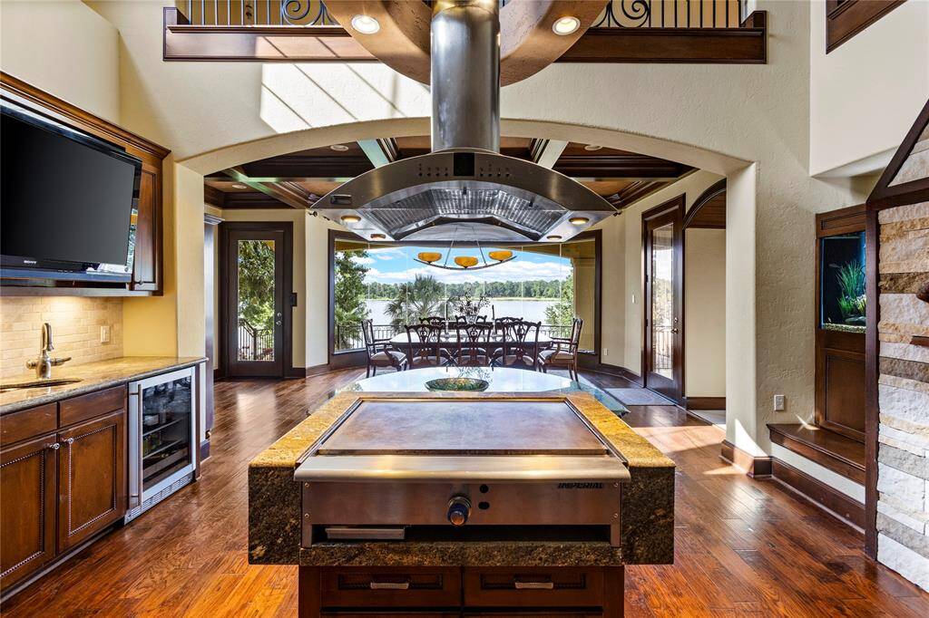 This is a spacious, modern kitchen featuring stainless steel appliances, a large island with a cooktop, and wooden cabinetry. It opens up to a dining area with a beautiful outdoor view, perfect for entertaining.
