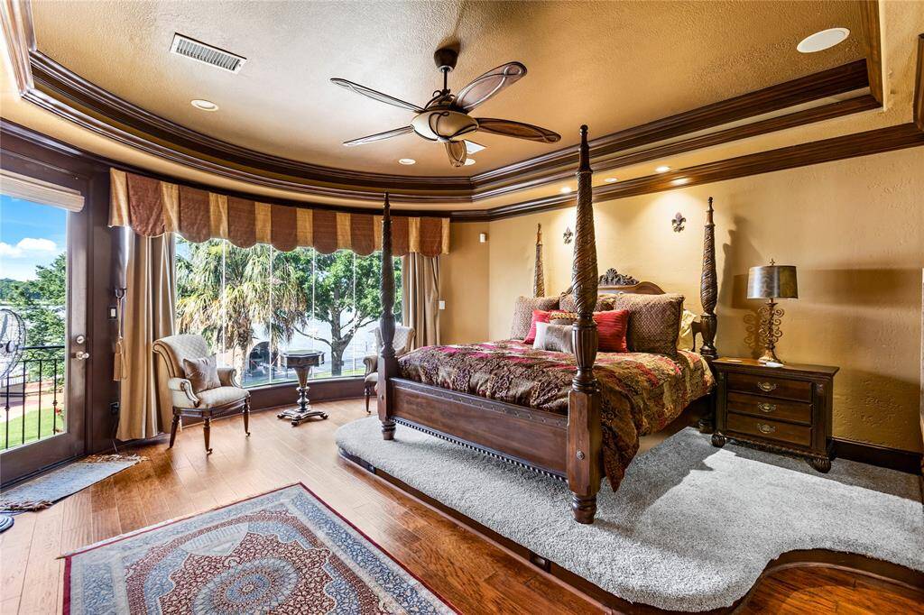 This is an elegantly appointed primary bedroom with raised floor, hardwood floors, and a curved wall of windows with a view. The room includes a sitting area and direct access to an outdoor space, enhancing its open and airy ambiance.