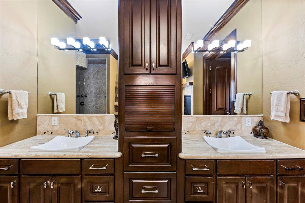 This is a well-appointed bathroom featuring dual vanities with ample storage, modern fixtures, and a view into a walk-in shower, all complemented by warm lighting and elegant finishes.
