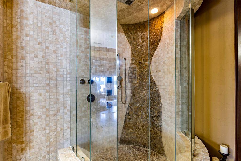 This is a modern walk-in shower featuring mosaic tile work, a curved glass door, and a sleek handheld showerhead, creating an elegant and luxurious bathroom experience.