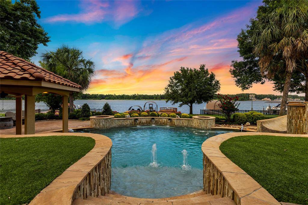 Mediterranean-style two-story home featuring a stucco exterior with a tile roof, arched entryway, and beautifully landscaped front yard, all set overlooking Lake Conroe.