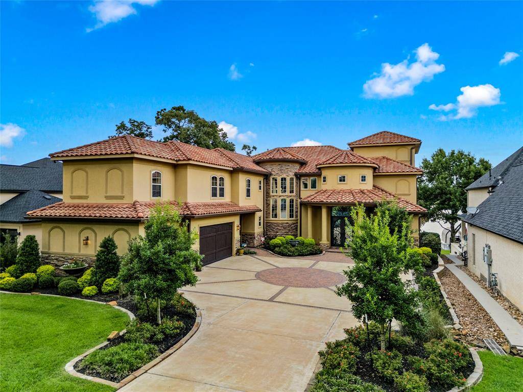 This photo showcases a luxurious two-story Mediterranean-style home with a terra cotta tile roof, a spacious driveway, and an oversized, side load, 3 car garage, set within a well-manicured landscape.