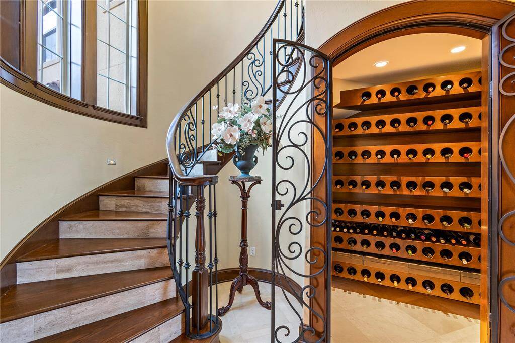This is an elegant interior space featuring a curved wooden staircase with ornate wrought-iron railings, complemented by a built-in wooden wine rack behind a decorative iron gate, adding a touch of sophistication and luxury perfect for wine enthusiasts.