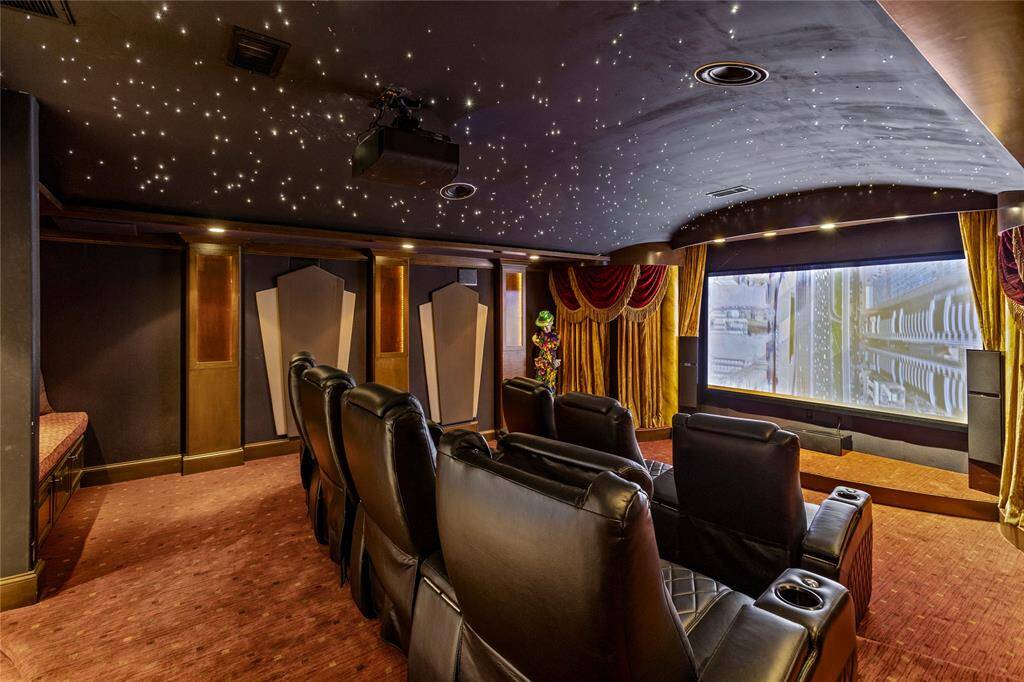 This is a luxurious home theater room featuring tiered leather seating, an expansive screen with heavy drapes, elegant wall panels, and a starlight ceiling for an immersive viewing experience.