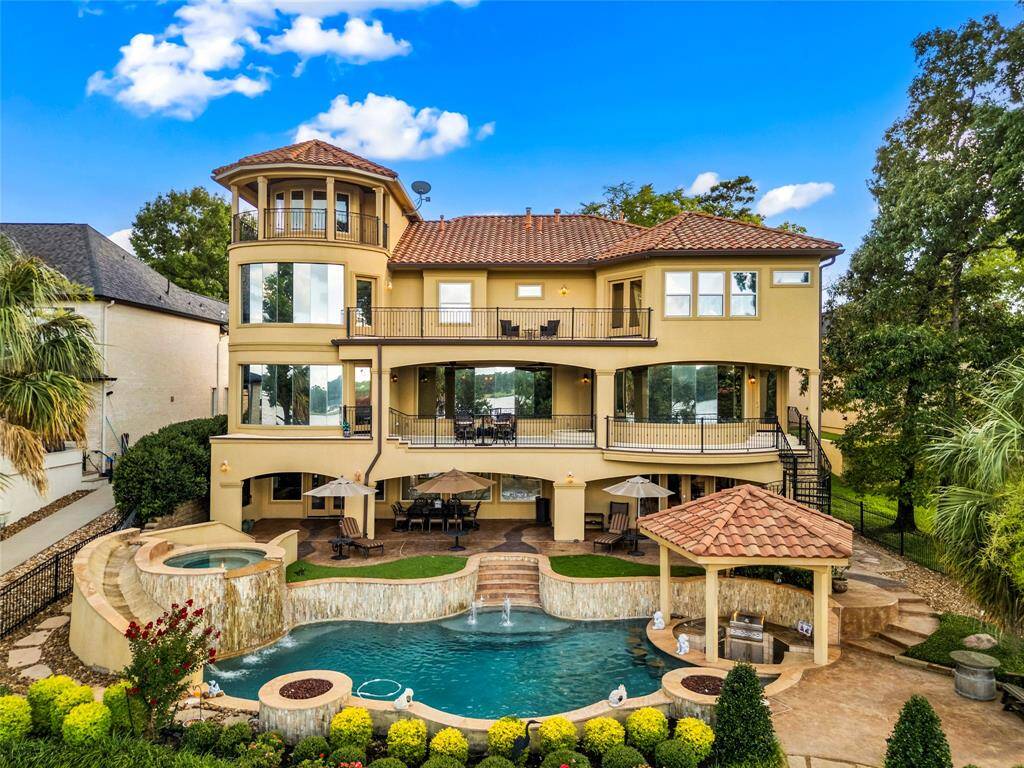 This is a luxurious 4-story home with a tiled roof, featuring expansive balconies, large windows, and an outdoor entertainment area with a swimming pool, hot tub, and covered patio space. Tropical backyard landscaping offers a relaxing retreat.