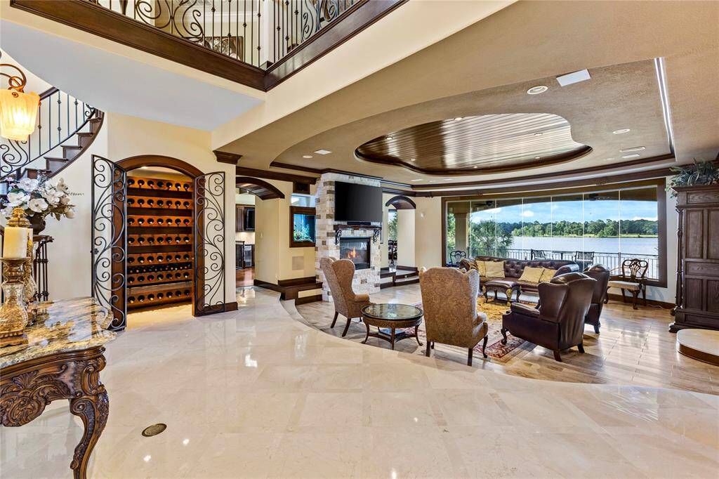 This is an elegant, open-plan living space with high ceilings, a grand staircase, and a sophisticated wine storage feature. The room opens up to a beautiful outdoor view, providing a seamless indoor-outdoor living experience.