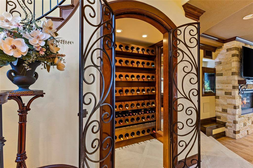 This is an elegant wine room featuring a built-in wine rack with ample bottle storage, framed by a beautiful arched entryway and ornate iron gates. The space is accented with stone wall details and warm lighting, creating a sophisticated ambiance for wine enthusiasts.