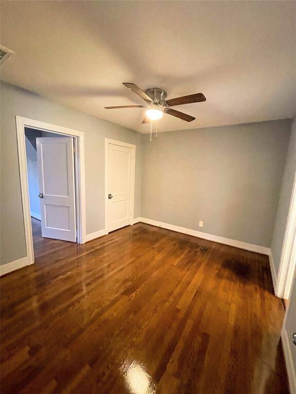 Bright bedroom with polished hardwood floors, light gray walls, and a ceiling fan and access to a en-suite.
