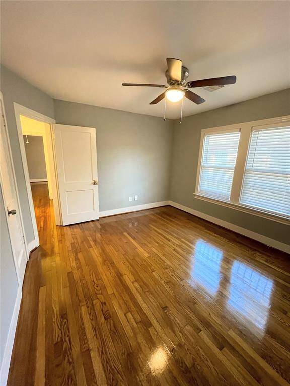 Another bright bedroom featuring polished hardwood floors and a ceiling fan. Natural light streams in through two windows, creating a cozy and airy atmosphere.