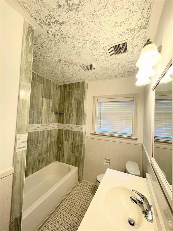 This primary bathroom features a modern design with a tiled shower and bathtub, textured ceiling, and a single-sink vanity. It has neutral tones and a window for natural light.
