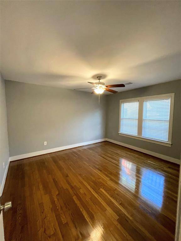 A third bedroom features polished hardwood floors, neutral walls, and a ceiling fan with light all creating a bright and inviting space.