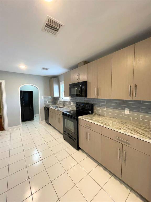 This kitchen features modern cabinetry with ample storage, sleek countertops, and a stylish tile backsplash. Equipped with black appliances, it has a clean, contemporary look with a spacious layout and tiled flooring.