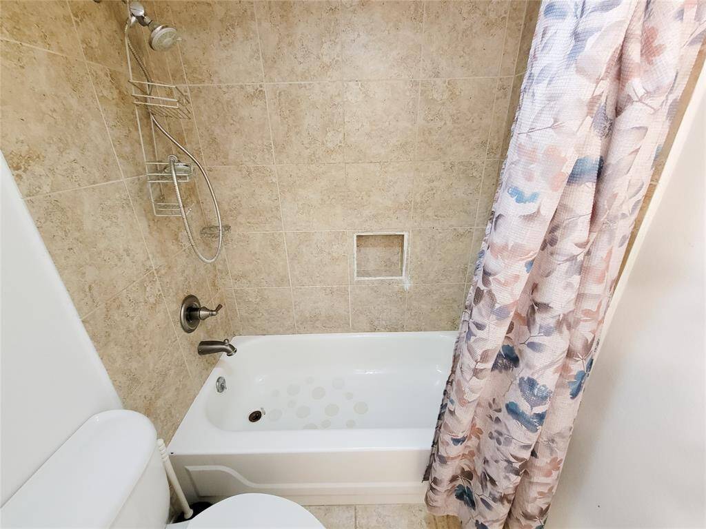 Bathroom with a full tub and shower combo, featuring beige wall tiles. A built-in shelf for toiletries.