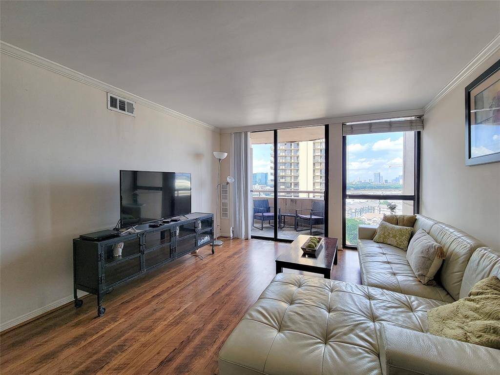 Large windows offer ample natural light and direct access to a private balcony with impressive city views. The room is furnished with a comfortable seating area and a TV stand, creating a cozy environment for relaxation.