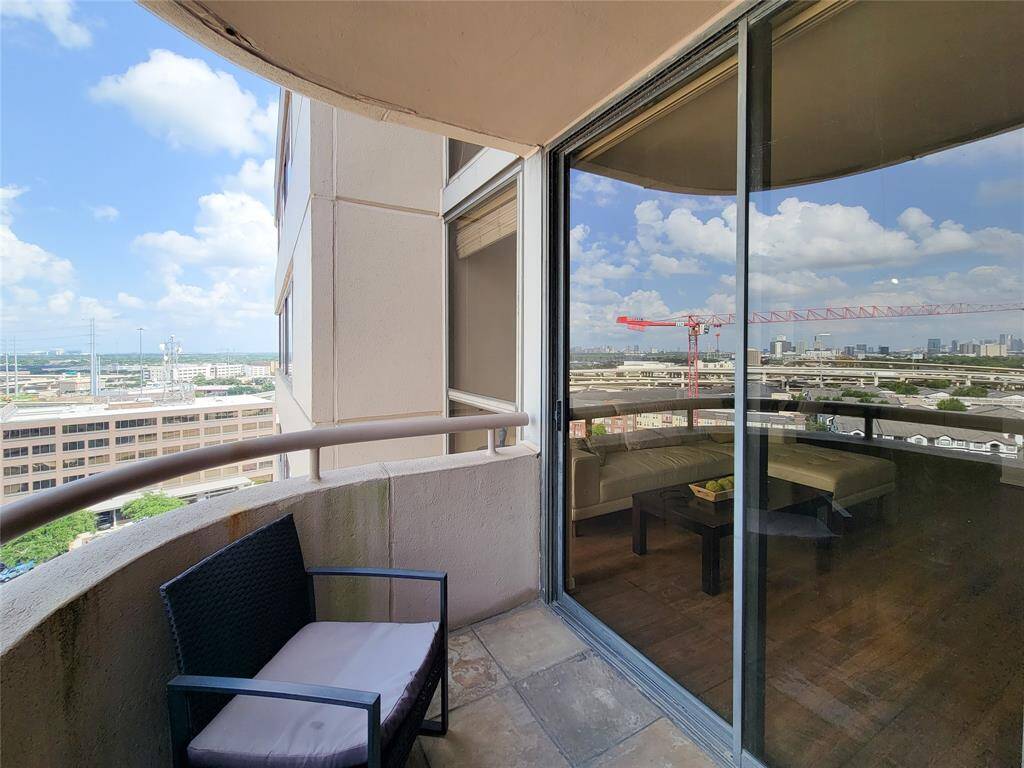 High-rise apartment balcony offers city views, with space for seating. The sliding glass door from the living area reflects the view!