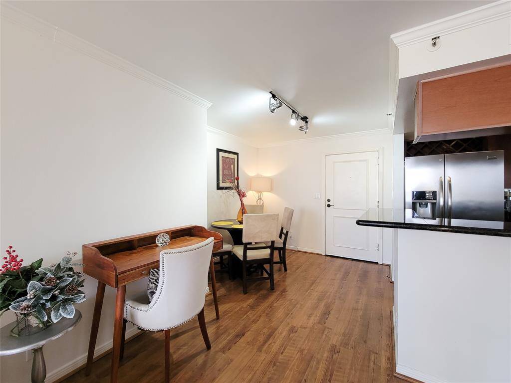 Well-lit, open-plan space featuring a dining area with a table and chairs, a small desk setup, and a view into the kitchen with modern appliances.