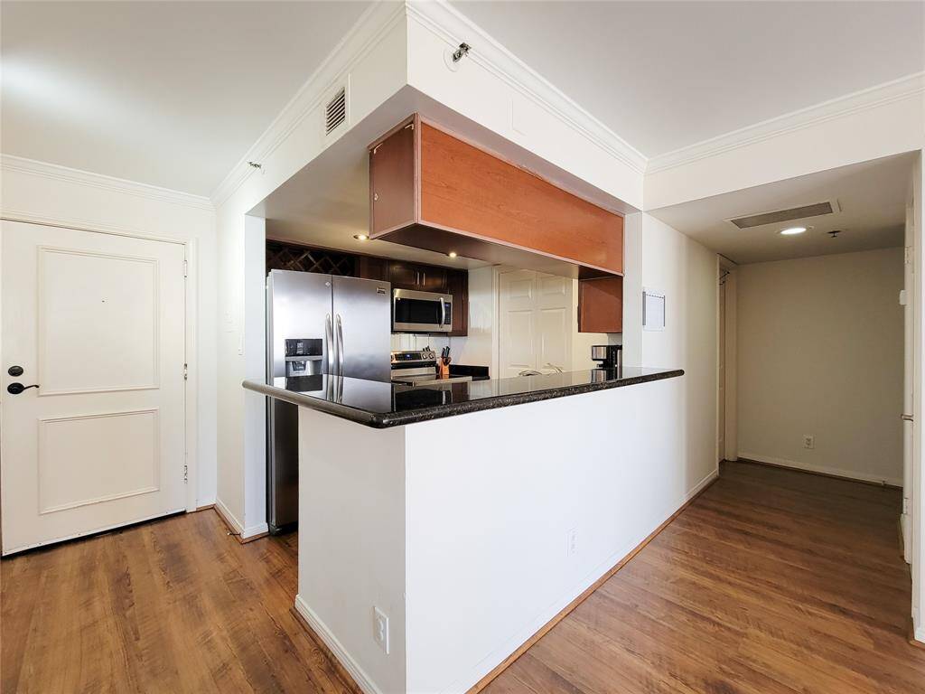Modern kitchen with stainless steel appliances and granite countertops, is open to the spacious, well-lit living area with white walls, offering a clean and contemporary living space. Hallway leading to the bath and bedroom, also has a hall closet.