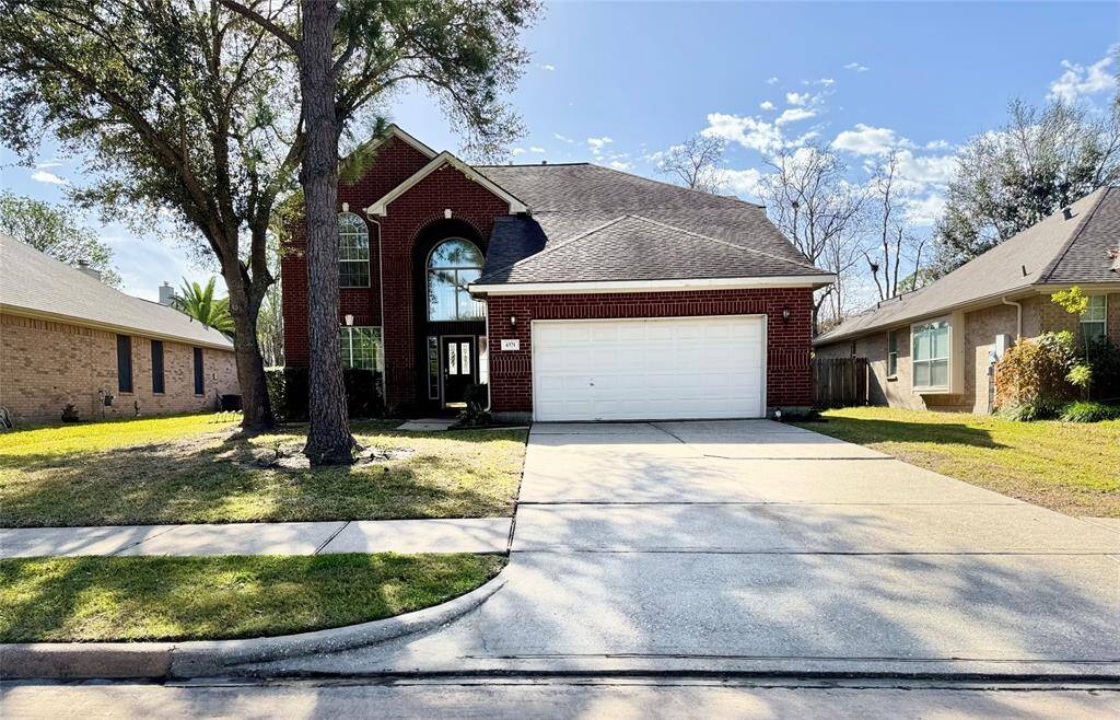 Two-story brick home with a double garage, set on a well-maintained lot. The house features a large driveway and mature trees, providing a welcoming curb appeal in a suburban neighborhood.