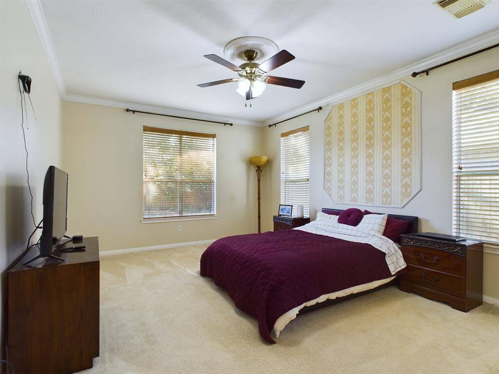 The large primary on-suite features a cozy carpeted floor, a ceiling fan, and ample natural light.