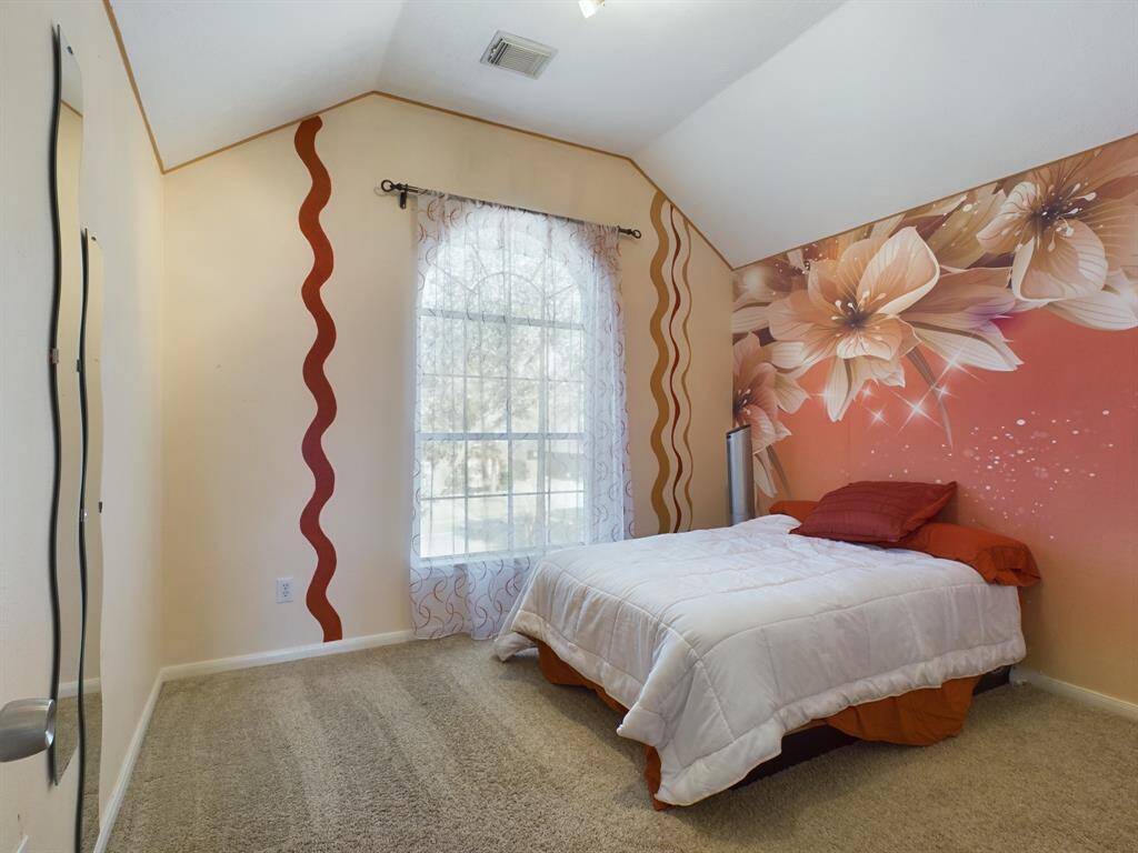 This cozy bedroom features a vaulted ceiling, carpeted floor, and a large window