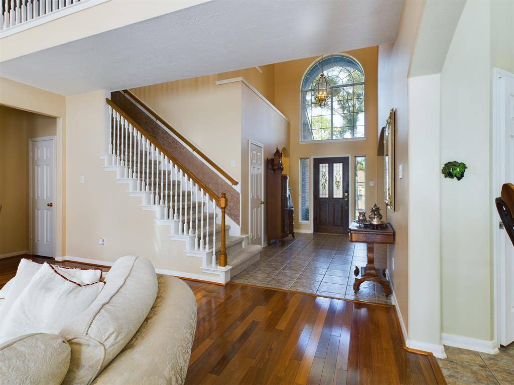 Features a wooden staircase with white spindles, hardwood floors, and a tiled section leading to the door.