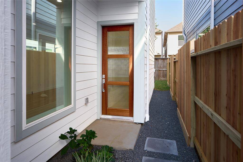 A sleek, modern front entry framed by clean lines, natural wood, and privacy offering a warm welcome home.