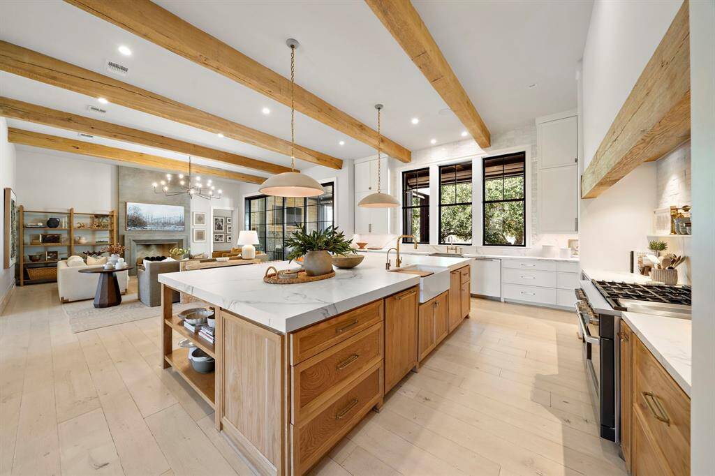 This stunning home features a classic farmhouse design with a spacious front porch, beautiful stone accents, and large windows. It's set against a picturesque backdrop with a well-maintained lawn and mature trees, offering a serene and inviting atmosphere.